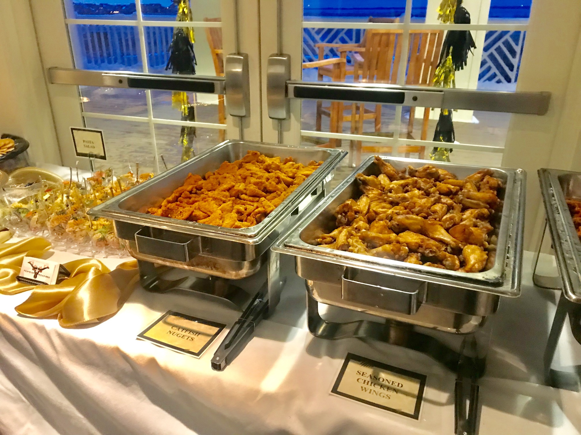 Chafing dishes of catfish nuggets and seasoned chicken wings on a catered buffet