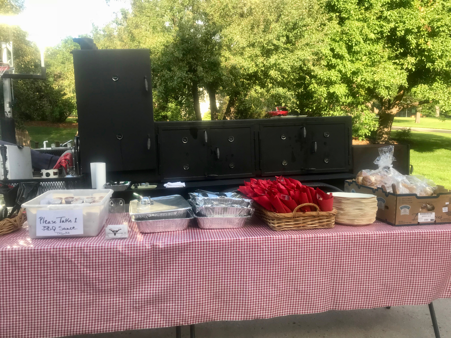 Outdoor catering setup with the custom offset smoker and gingham-covered serving table
