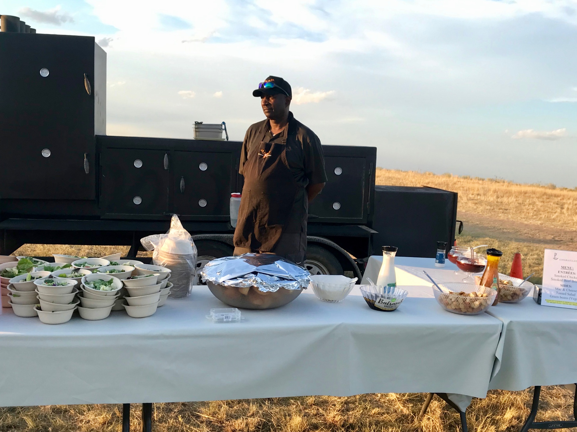 Pit master beside the smoker at an outdoor country wedding setup