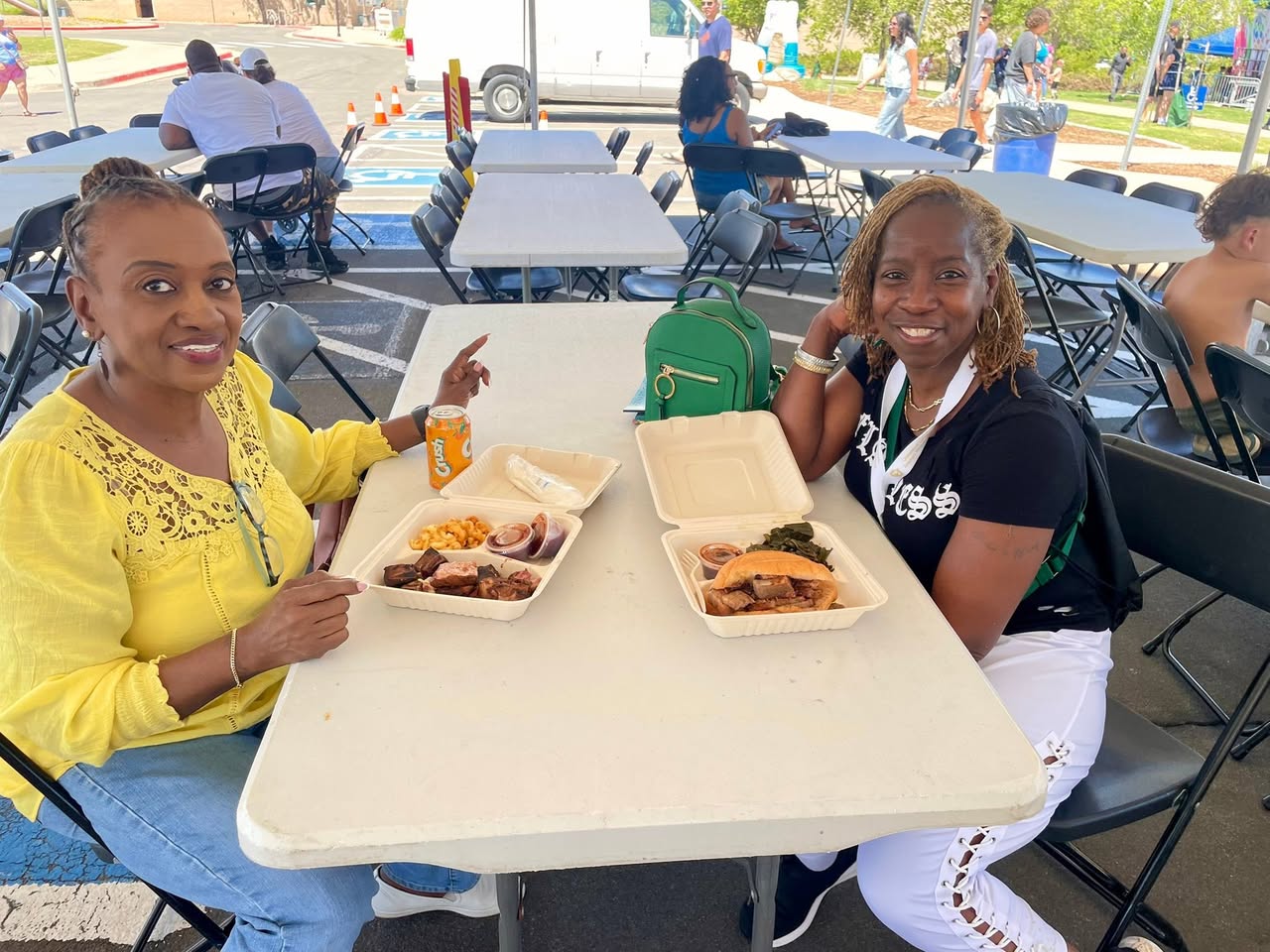 Two guests enjoying brisket, collard greens and mac & cheese plates at a global festival