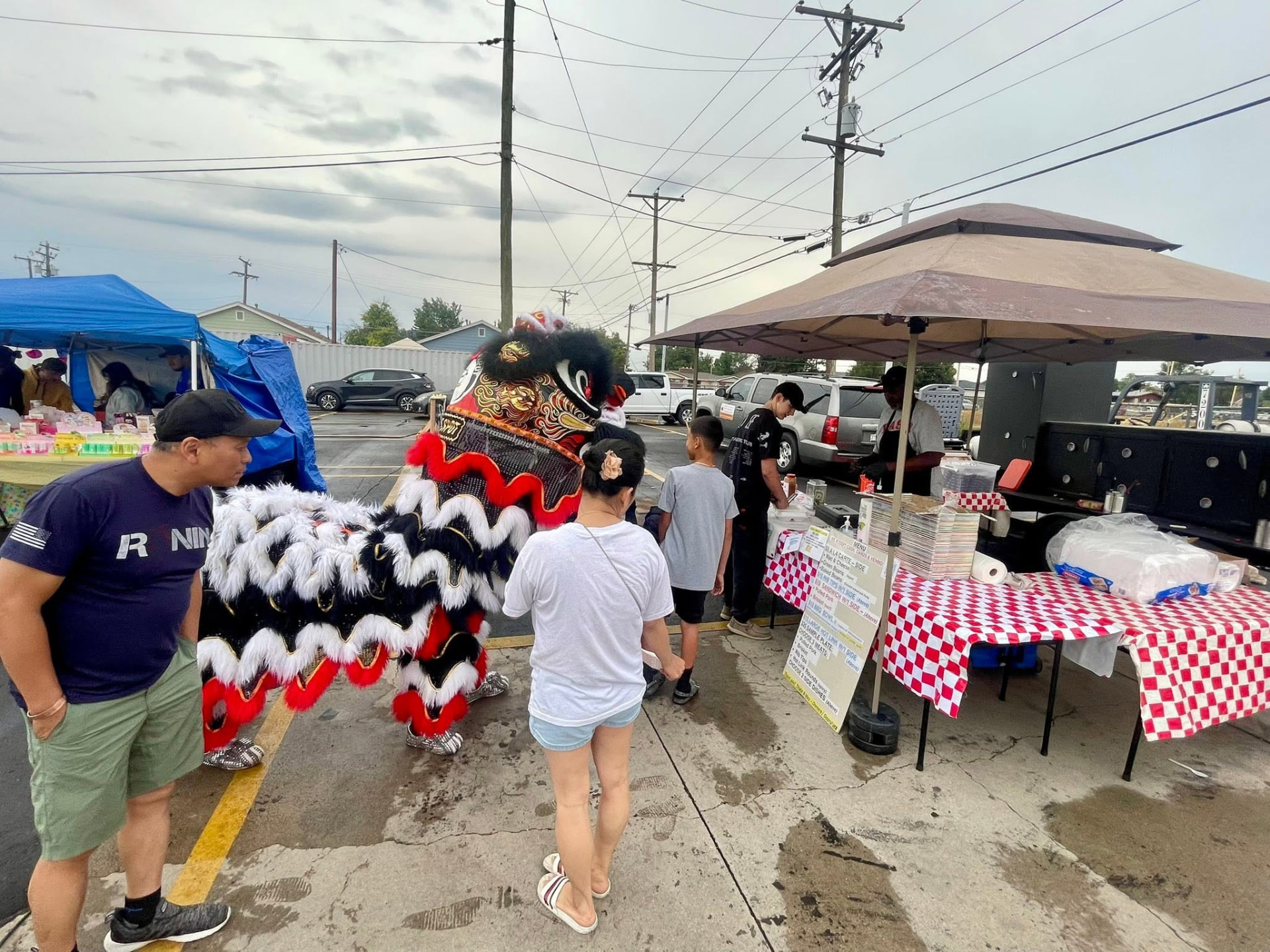 Market place vending setup with customers and a lion dance performance passing by