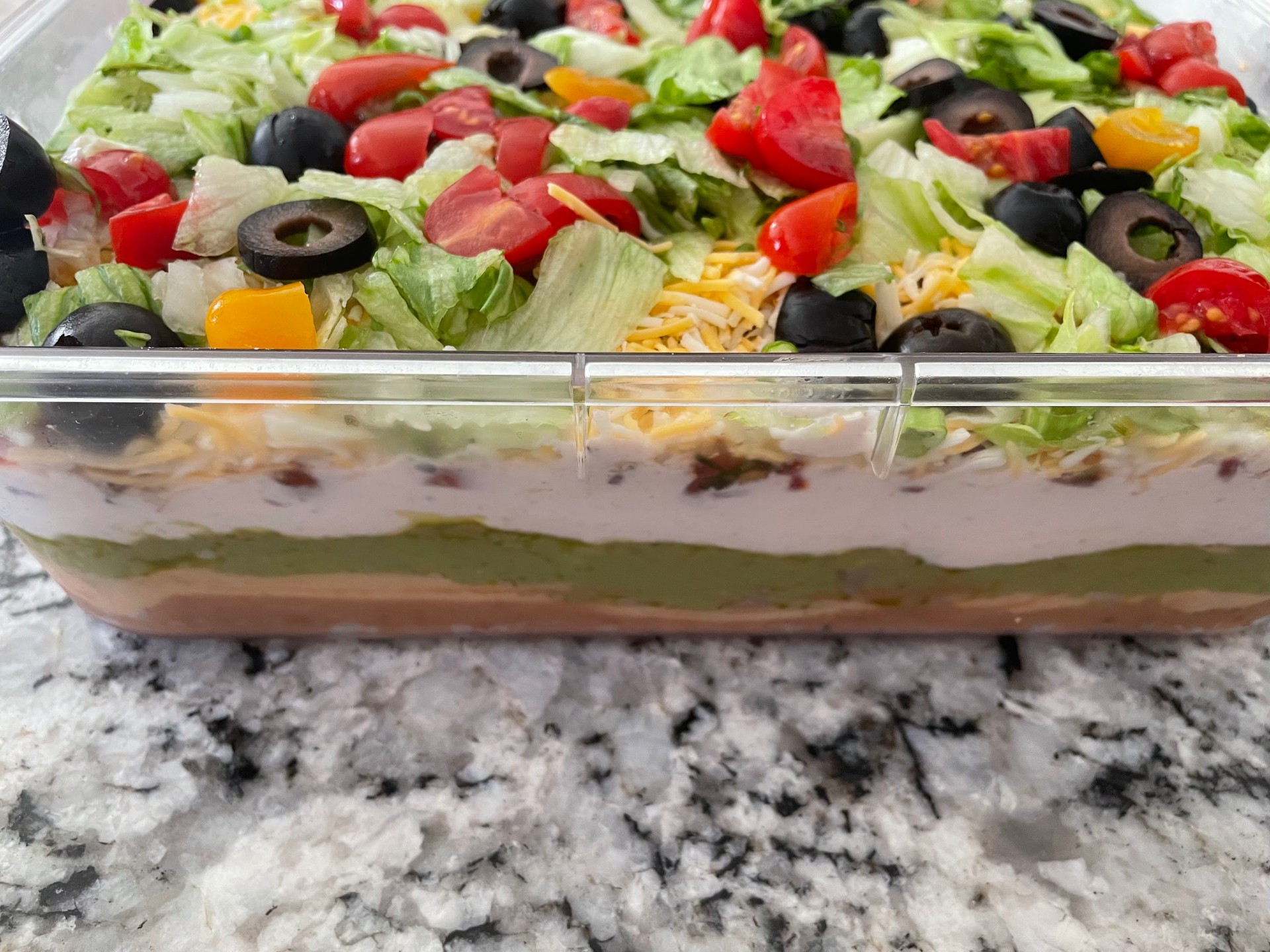 Seven layer dip with lettuce, tomatoes, olives, cheese, and beans
